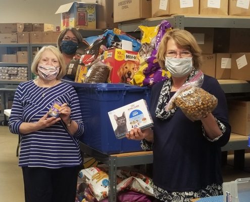 Women stand in a warehouse with a bin of prepackaged pet food