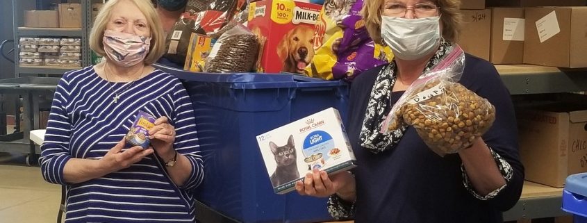Women stand in a warehouse with a bin of prepackaged pet food