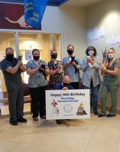 a group of men and women in scrubs stand holding cats, while wearing face masks. A man kneels in front holding a sign with a cat and dog on it saying "happy 70th birthday Blue Ridge Humane Society"