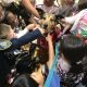 A dog sits in the middle of a group of children as they reach to pet her.