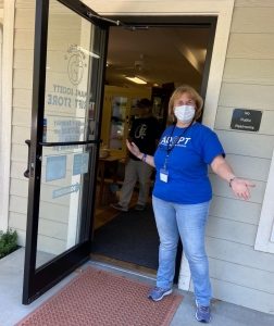 a women wearing a mask stands by an open door with a welcoming stance