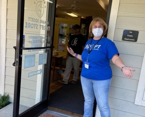 a women wearing a mask stands by an open door with a welcoming stance