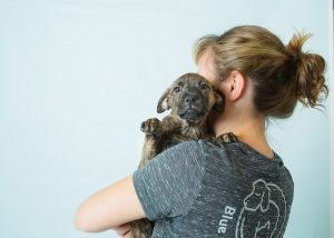 a puppy with it's face towards the camera is held by a women facing away from the camera