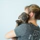 a puppy with it's face towards the camera is held by a women facing away from the camera