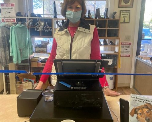 a woman wearing a mask stands behind a cash register