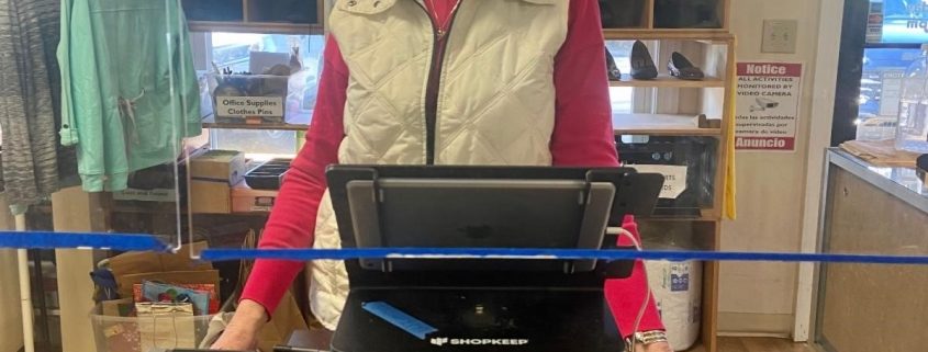 a woman wearing a mask stands behind a cash register