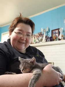 a grey kitten is held by a smiling lady