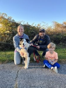 a women, man, and young child pose with a multicolored medium sized dog