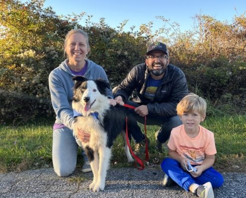 a women, man, and young child pose with a multicolored medium sized dog