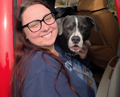 A woman in black glasses smiles with a black and white dog