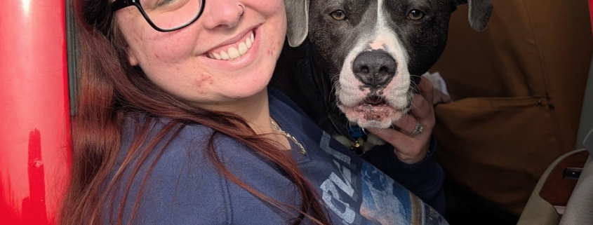 A woman in black glasses smiles with a black and white dog