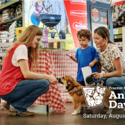 A person in a red vest pets a dog with a mother and child in the background