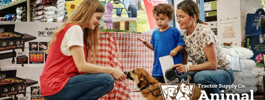 A person in a red vest pets a dog with a mother and child in the background